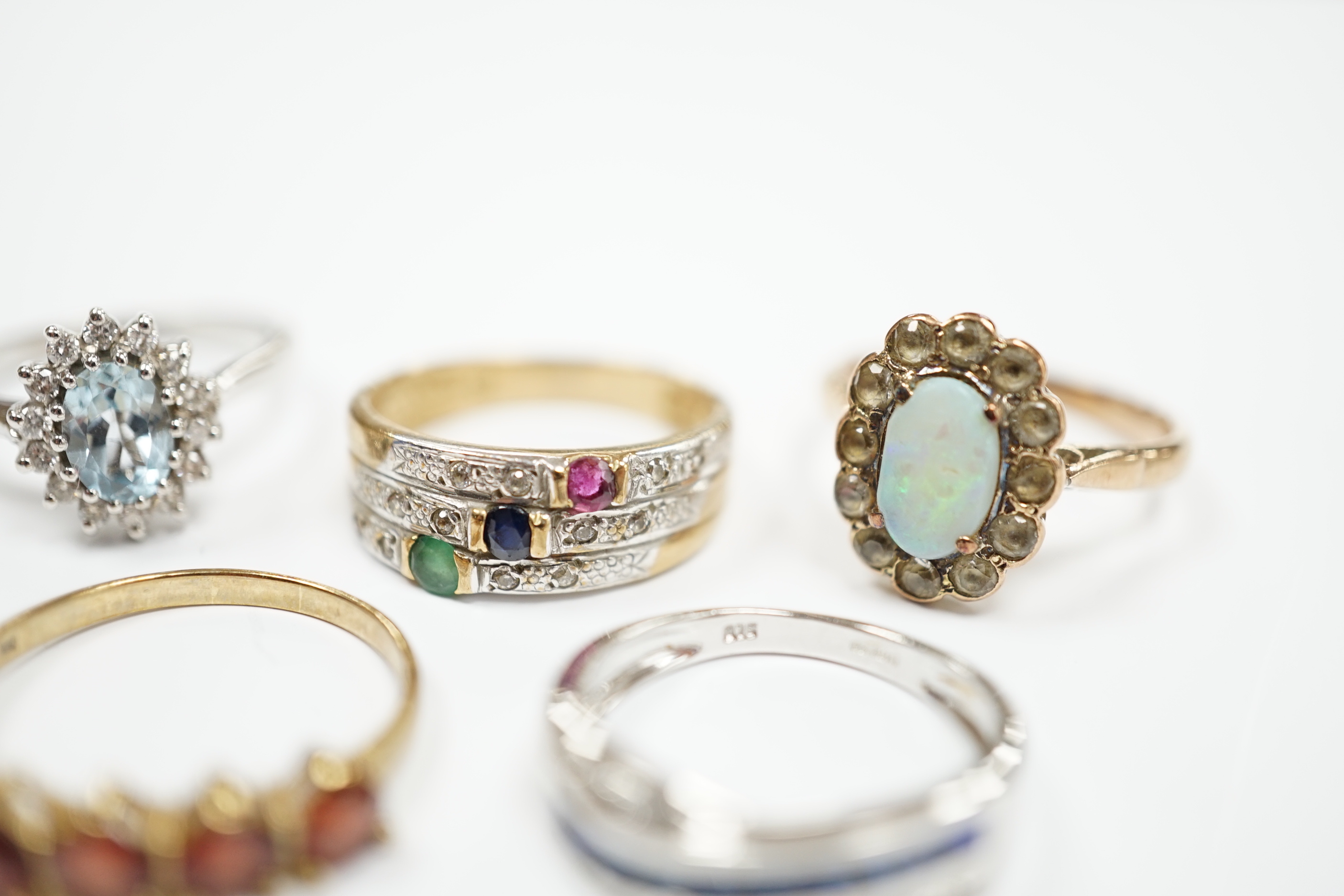 Four assorted 9ct and gem set rings, including opal and white sapphire?, blue topaz and diamond, sapphire and diamond chip crossover and five stone garnet? and a yellow metal and four colour cubic zirconia ring, gross we